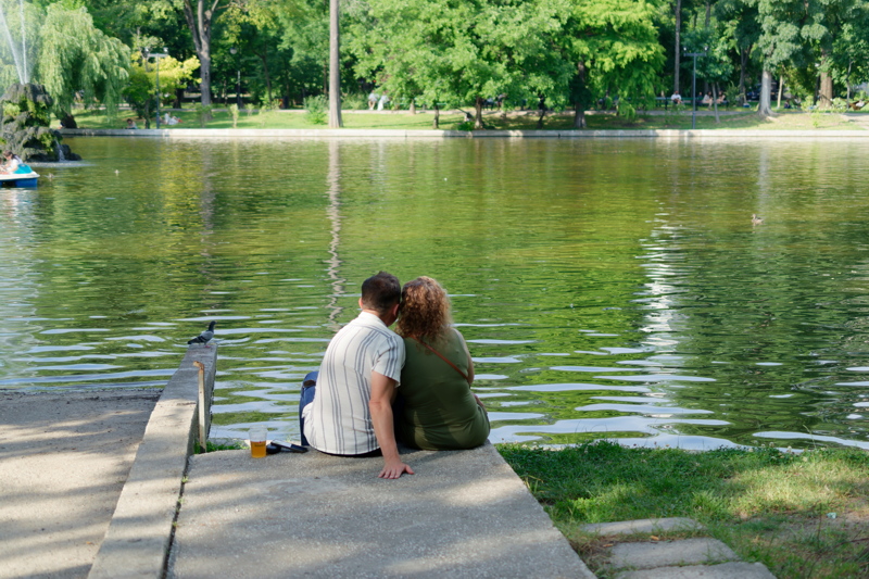 16 - Young couple sitting together by a calm lake in a park